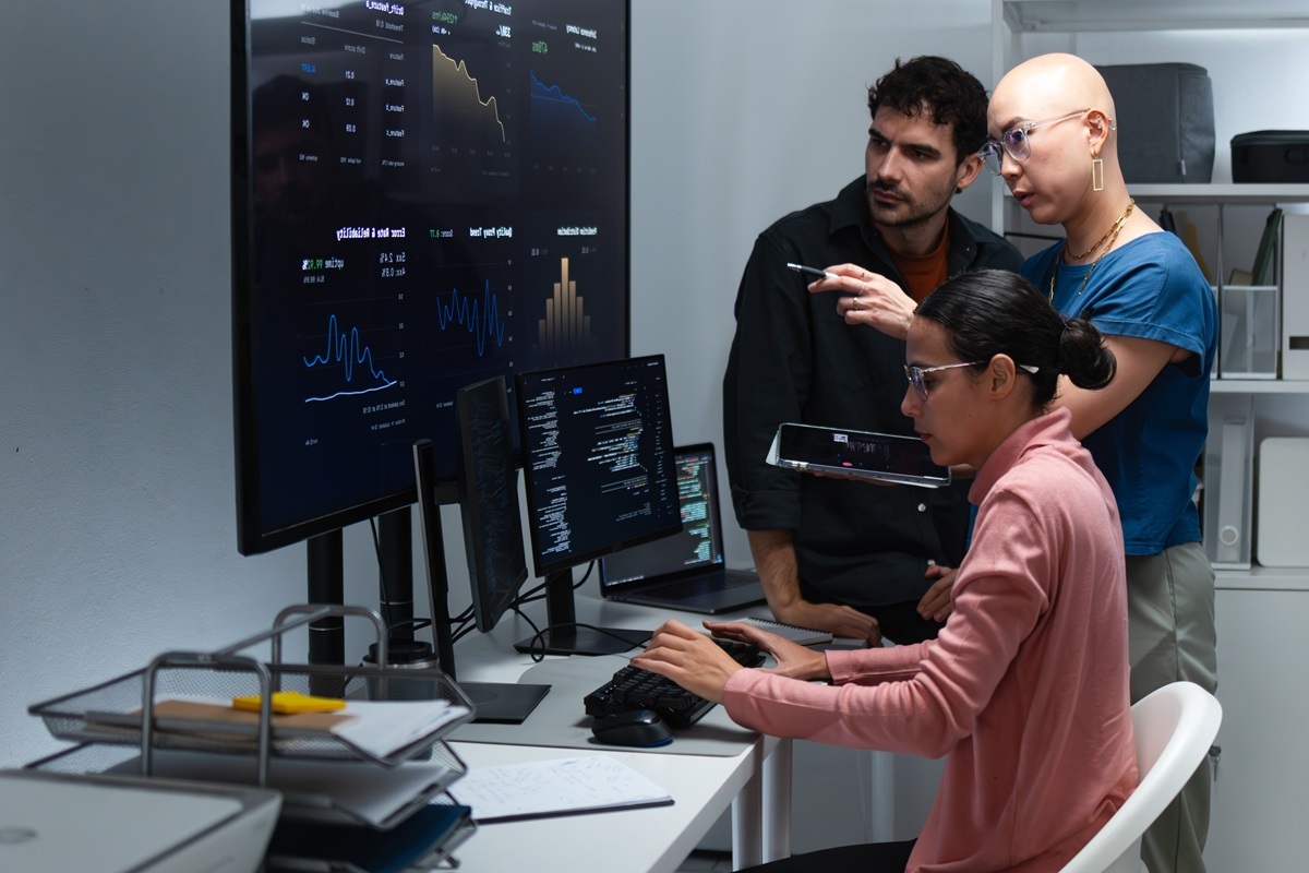 DevOps Team Checking Monitoring Data and Application Trends, Reviewing Operational Metrics, Analyzing Observability Metrics on Large Screen in Control Room at Office.